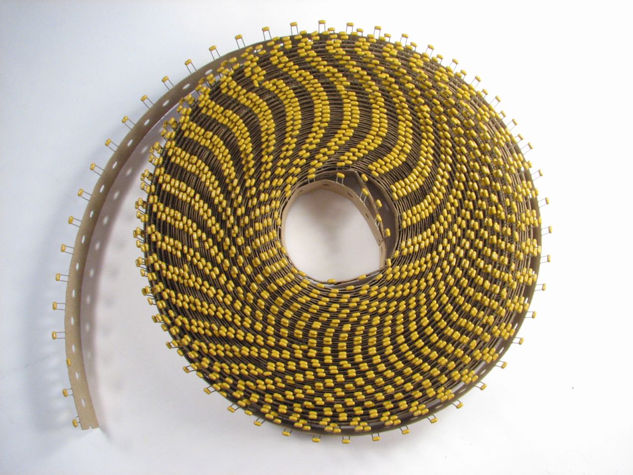 Figure 3 — A paper-tape "ammo pack" roll of ceramic chip capacitors. MLCCs are handled, shipped, and placed by the reel — often tens of thousands to a reel — which is why the value lives on the ree…