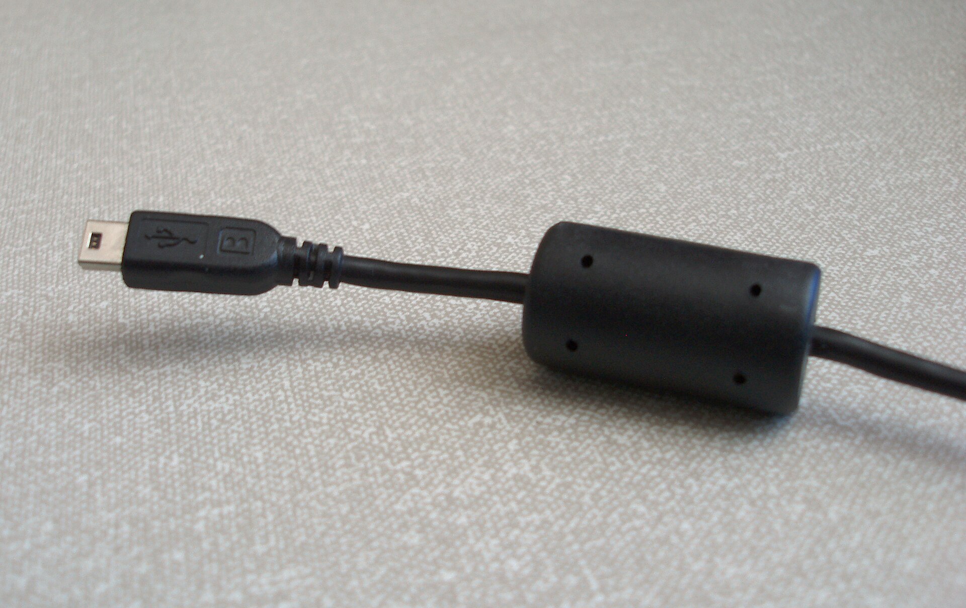 Figure 7 — A clamp-style ferrite core moulded onto a USB cable. The lossy ferrite acts on common-mode noise trying to travel along the cable, turning it to heat; because it is specified by impedanc…