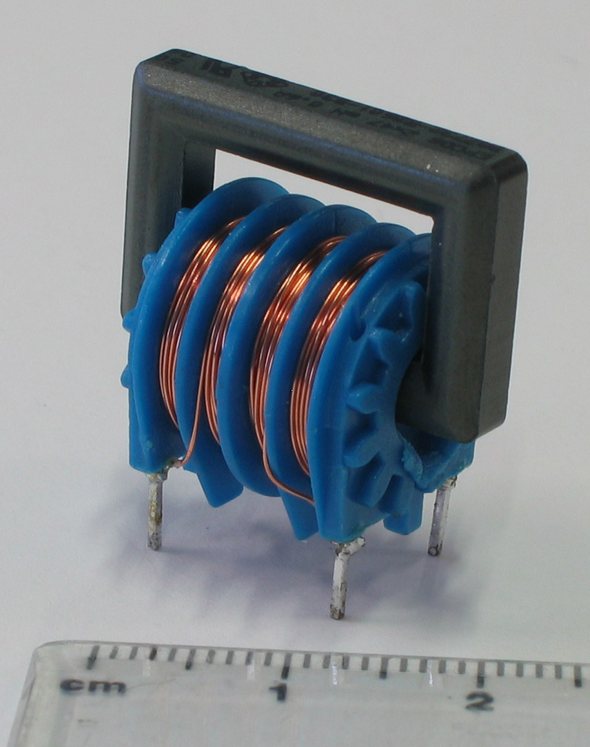 Figure 8 — A wound common-mode choke on a two-section bobbin over a ferrite E-core: the two windings kept in separate chambers, the physical embodiment of Project 4's mains-choke arrangement. Ruler…
