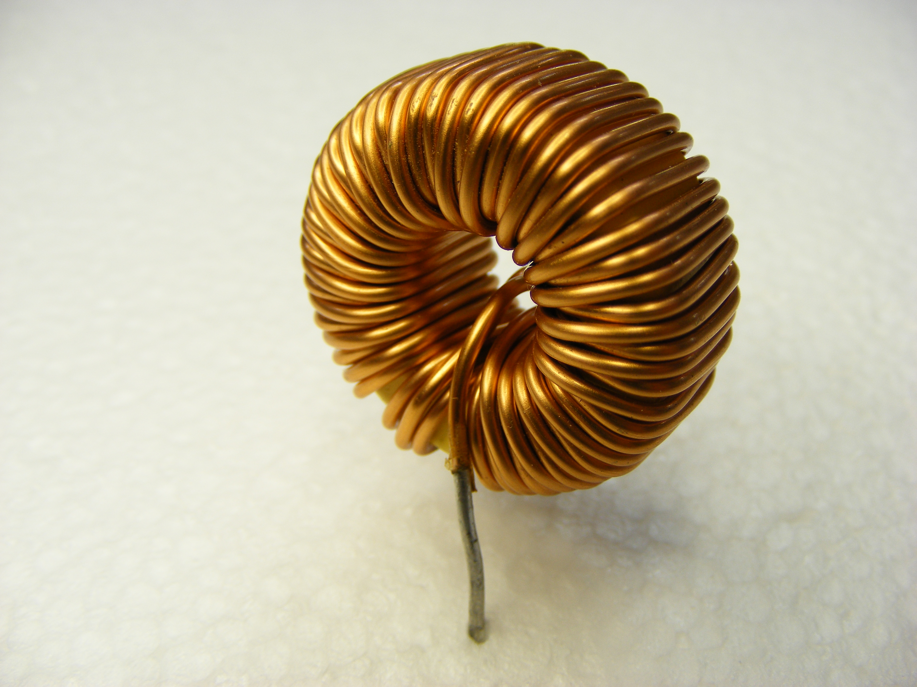 Figure 7 — A toroidal inductor: enamelled copper wound close and even around a ring core. The ring geometry keeps almost all of the magnetic flux inside the core, so a toroid radiates little interf…
