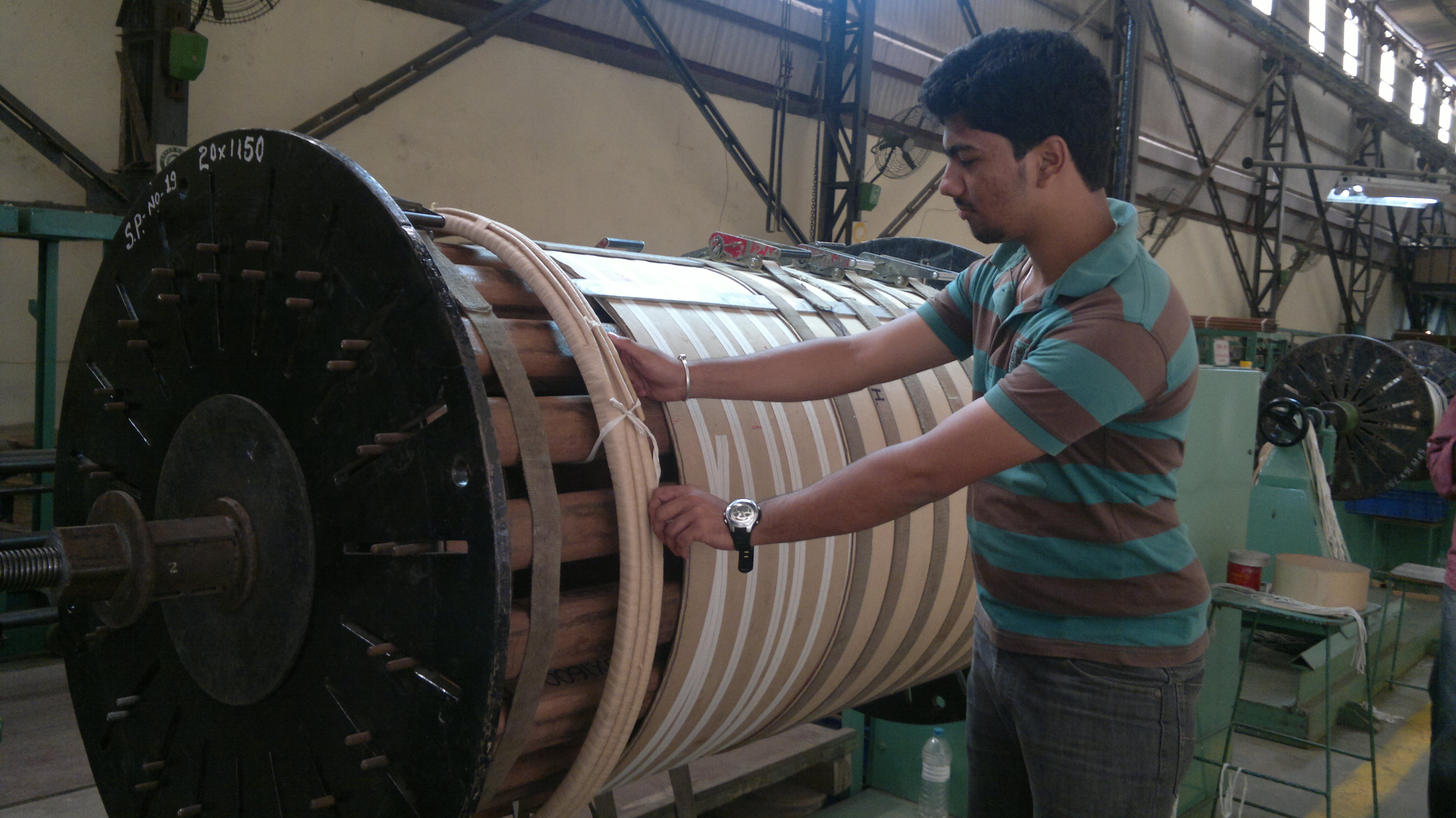 Figure 7 — Large-scale winding: a power-transformer coil being built up on a vertical winding machine, its lead-screw traverse visible at lower left and the paper-insulated conductor feeding from a…