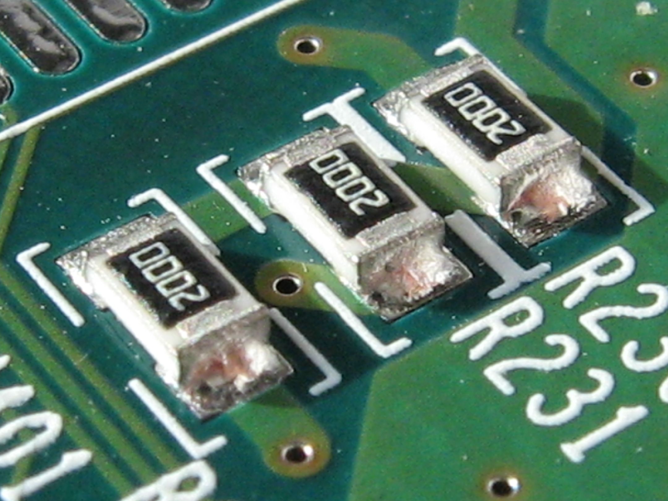 Figure 4 — Three thick-film chip resistors soldered to a board, marked "2000" (a 3-digit code for 200 Ω: two significant figures, then zero zeros). The black body is the glass overglaze; the bright…