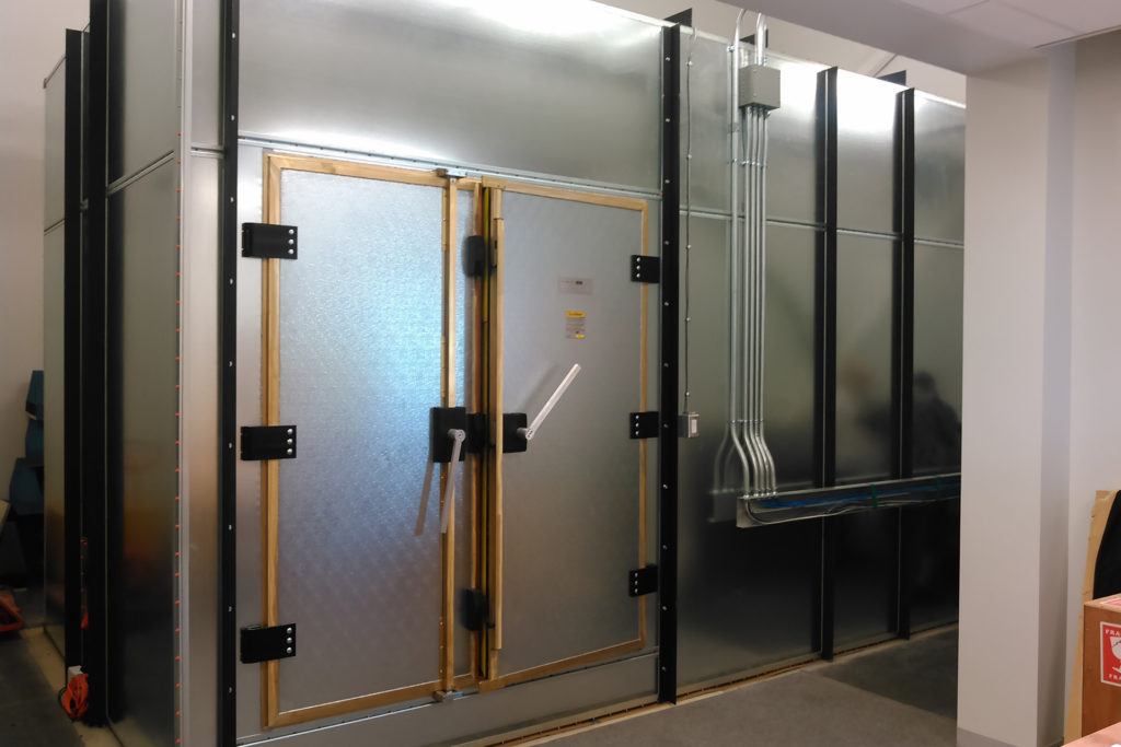 Figure 9 — The inside of a knife-edge shielded double door. The bronze/beryllium-copper fingerstock runs around the door frame; the wooden batten protects the delicate knife-edge and fingerstock fr…