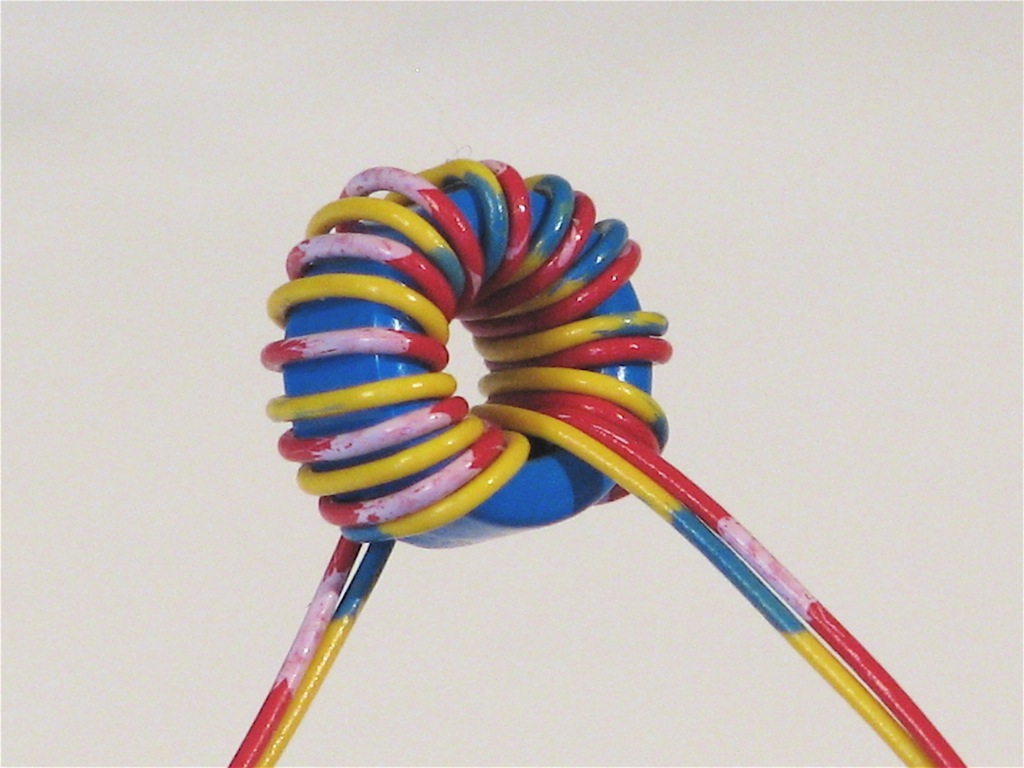 Figure 6 — A small toroid wound by hand. Where the core's hole is too small to admit a shuttle, the winder threads the wire through turn by turn — the case for most little RF and signal toroids, an…