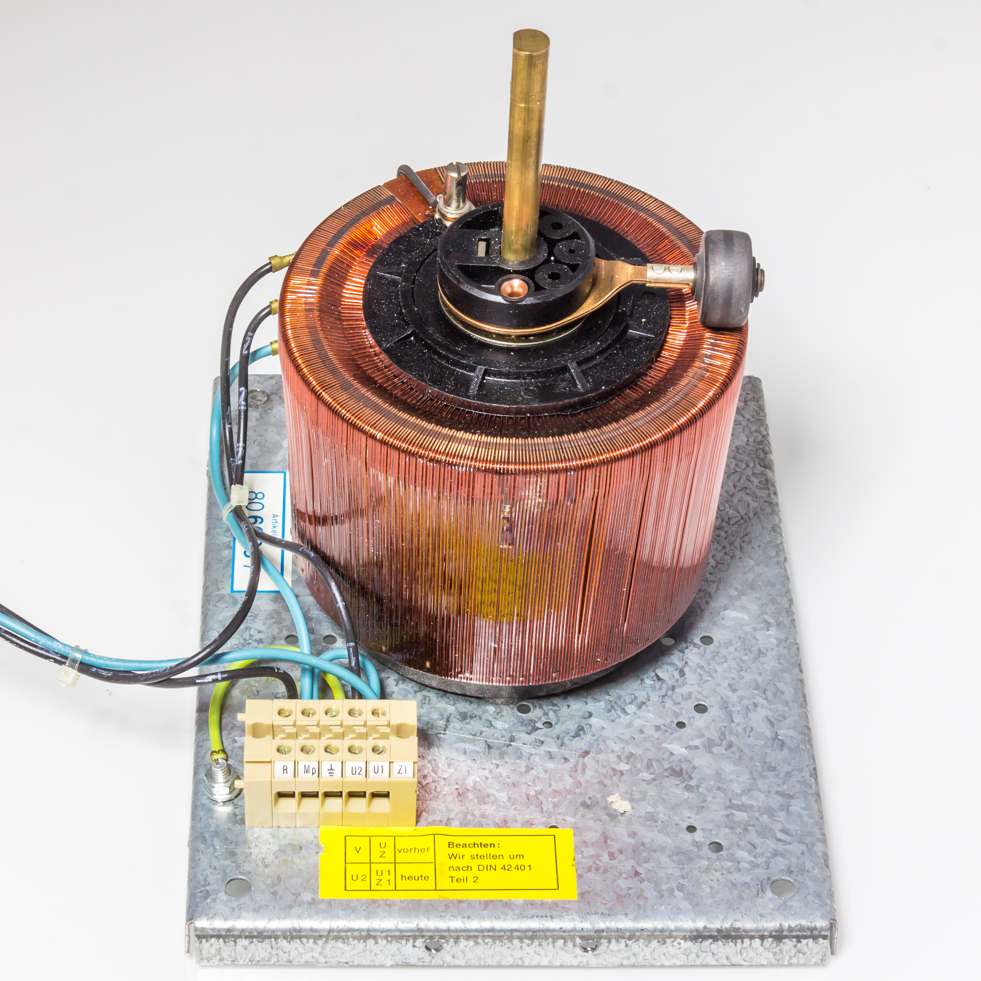 Figure 4 — A Variac (variable autotransformer): a single-layer winding on a toroidal core with a bared track along the top, swept by a carbon brush on a rotating brass arm. Turning the shaft taps t…